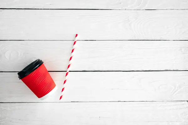 Red paper cup and straw for drinks on a white wooden background. View from above. Space for text.
