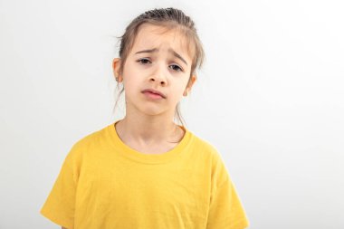 Sarı tişörtlü küçük beyaz kız, beyaz arka planda yalnız, yorgun, ilgisiz, kopya alanı olan bir çocuktan memnun görünmüyor..