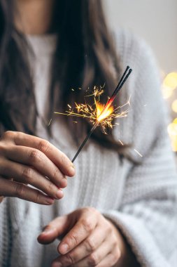 Elinde maytap tutan gri kazaklı bir kadın, yakın plan, Noel kutlaması konsepti..