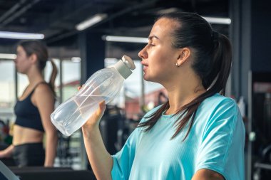 Spor salonunda koşu bandında kardiyo çalışmasından sonra su içen bir kadın..