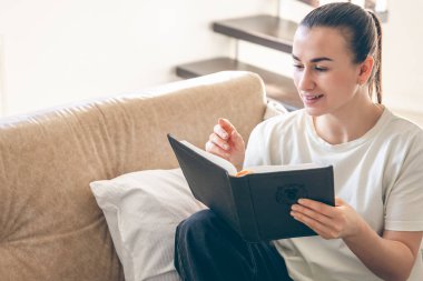 Evde kitap okuyan genç beyaz bir kadın. Bir kadın kanepede kitap okuyor. Hobiler, boş zaman ve iyi bir okuma alışkanlığı, kopyalama alanı..