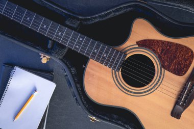 Koruyucu durumda akustik gitar ve kalem, üst görüş ve müzik öğrenme kavramına sahip not defteri.