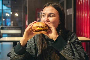 Fast food kafede tavuk burger yiyen çekici genç bir kadın. Sağlıksız yüksek kalorili yemek ve fast food..