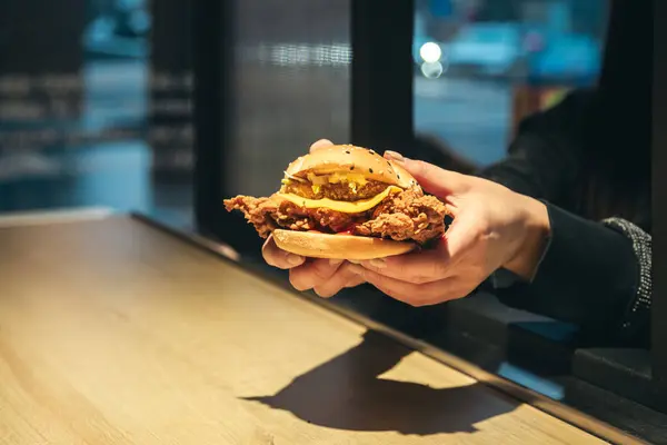 An appetizing chicken burger in female hands in a fast food restaurant. A woman holds a burger in her hands to order to go. Copy space.