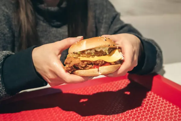 Burger with fried chicken in a fast food cafe in female hands. Healthy high-calorie food and fast food.