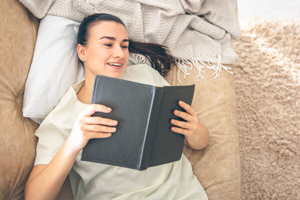Вид сверху на счастливую женщину, лежащую на диване в своем уютном доме и читающую книгу, копировальное пространство.