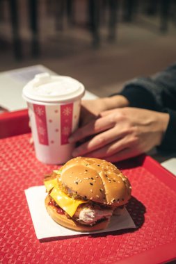 Fast food kafede kızarmış tavuklu burger, kadınların elinde. Sağlıklı yüksek kalorili yemek ve fast food..