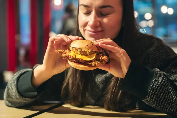 Attractive young woman eating a chicken burger in a fast food cafe. Unhealthy high-calorie food and fast food.