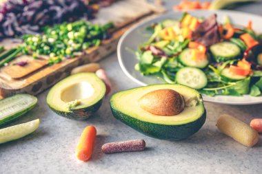 Avokado yarımları mutfak masasında taze sebzelerle. Vejetaryen salatası pişiriyorum. Sağlıklı beslenme.