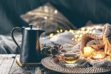 Bir çaydanlık, bir fincan çay, yanan mumlar ve odanın arka planında örülmüş bir element ile rahat ev kompozisyonu. Konforlu ev kavramı.
