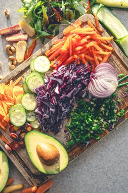 Mutfak masasının üzerindeki kesme tahtasının üzerinde taze sebzeler, üst manzara. Avokado ve diğer sebzeler salatayı hazırlarken. Sağlıklı beslenme ve vejetaryenlik kavramı.