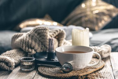 Bir fincan çay, mum ve odanın iç kısmının bulanık arka planında örülmüş bir element ile rahat ev kompozisyonu.
