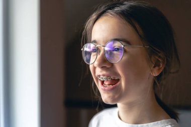 Evde gözlüklü ve diş telli genç bir kızın portresi. Ortodontik tedavi kavramı.