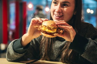 Fast food kafede tavuk burger yiyen çekici genç bir kadın. Sağlıksız yüksek kalorili yemek ve fast food..