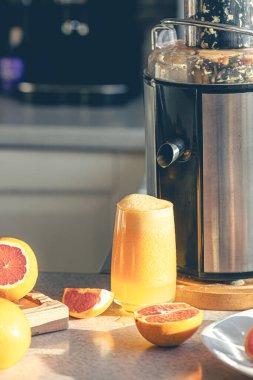 Mutfak masasındaki bardakta taze portakal suyu. Elektrikli meyve sıkacağı kullanarak taze portakal suyu hazırlıyorum..