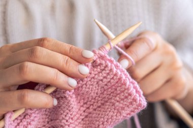 Pembe yün kazak ören kadın ellerinin yakın çekimi. Kız hobileri için içeri giriyor. Örgü konsepti.