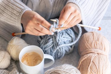 Gri iplikle örgü ören bir kadın, yakın plan. Kış hobisi, ev konforu.