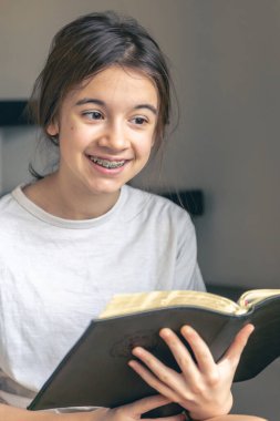 Genç bir kız kitap okuyor ve diş telleriyle dişlerini göstererek gülümsüyor. Ortodontik tedavi kavramı.