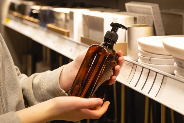 Close up, a dispenser for liquid soap in female hands in the store. Woman choosing soap bottle for bathroom at the interior market.