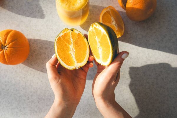 Halves of a fresh orange in female hands on the background of the kitchen table, top view. Preparation of natural juice at home.