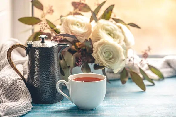 Bir fincan çay, bir çaydanlık ve pencerenin yanında çiçekler. Rahat ev kompozisyonu. Boşluğu kopyala.