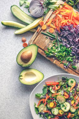 Mutfak masasının üzerindeki kesme tahtasının üzerinde taze sebzeler, üst manzara. Avokado ve diğer sebzeler salatayı pişirirken.