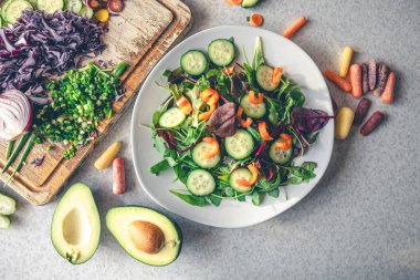 Mutfak masasındaki tabakta sebze salatası, üst manzara. Taze sebzelerden yapılmış vejetaryen salatası. Evde salata hazırlama süreci.