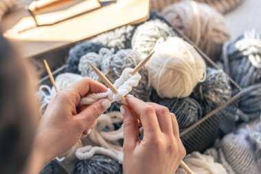 Kadın ellerinin yün kazak ördüğü yakın çekim. Kadın kalın iplikten örgü örüyor. El yapımı giysiler. Kız hobileri için içeri giriyor..