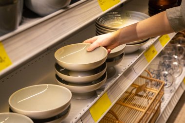 Ev eşyaları dükkanındaki bir raftan kadın el ele tutuşma kasesi. Seramik plakalı raflar bir sofra takımında satılıyor..