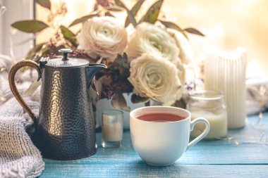 Bir fincan çay, bir çaydanlık ve pencerenin yanında çiçekler. Rahat ev kompozisyonu. Boşluğu kopyala.