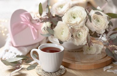 Bir fincan çay, pembe hediye kutusu ve beyaz çiçeklerle romantik kompozisyon. Sevgililer Günü için hala hayat var. Tebrik kartı tasarımı.