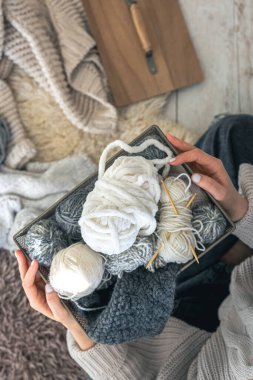 Yakın plan kadın elleri yün bir süveter giyer ve elinde iplik topları olan bir kutu taşır. Kadın örgü hobisi..