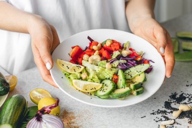 Mutfaktaki bayanların ellerinde taze sebze dilimlenmiş bir tabak. Sağlıklı yeme kavramı.