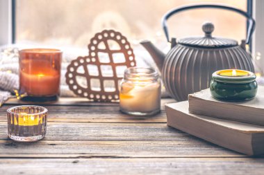 Kitaplarla, mumlarla ve pencerenin yanında çaydanlıkla dolu rahat bir arka plan. Ev konforunun detaylarıyla dolu bir hayat.