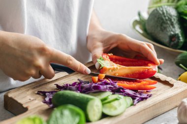 Bir kadın mutfaktaki tahta bir tahtada taze dolmalık biber kesiyor. Vejetaryen sebze salatası pişiriyorum. Yakın plan, sebze doğrayan eller..