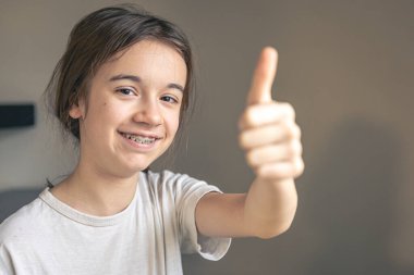 Diş teli takan genç bir kız evde gülümsüyor, dişlerini gösteriyor. Ortodontik tedavi kavramı.