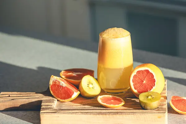 A glass of freshly squeezed juice and fruits on a wooden cutting board on the kitchen table. Squeezed fruit juice at home, copy space.