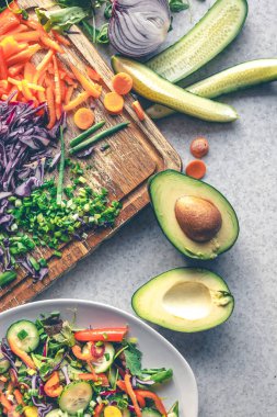 Mutfak masasının üzerindeki kesme tahtasının üzerinde taze sebzeler, üst manzara. Avokado ve diğer sebzeler salatayı pişirirken.