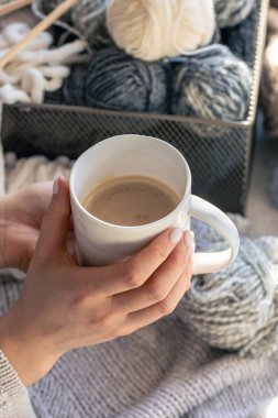 Kadın ellerinde bir fincan kahve ve iplik ipliği. Ev konforu, hobi olarak örgü örmek..