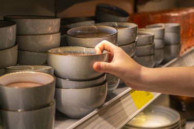 Ev eşyaları dükkanındaki bir raftan kadın el ele tutuşma kasesi. Seramik plakalı raflar bir sofra takımında satılıyor..