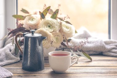 Bir fincan, çaydanlık ve ranunculus çiçekleri ile rahat bir kompozisyon. Boşluğu kopyala.