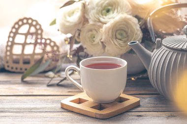 Bir fincan çay, çaydanlık ve ranunculus çiçeğiyle rahat ev kompozisyonu. Boşluğu kopyala.