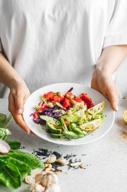 Mutfaktaki bayanların ellerinde taze sebze dilimlenmiş bir tabak. Biber salatası, lahana ve salatalık. Çiğ sebze salatası, vejetaryen..