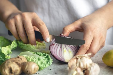 Bir kadın mutfak masasında salata için soğan doğruyor, yakın plan. Kadın elinde yarım soğan, sağlıklı bir yemek hazırlıyor..