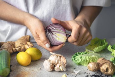 Bir kadın mutfak masasında salata için soğan doğruyor, yakın plan. Kadın elinde yarım soğan, sağlıklı bir yemek hazırlıyor..