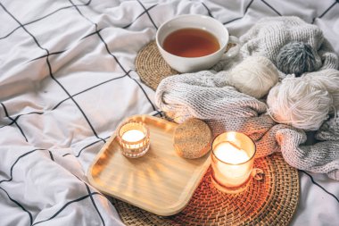 Bir fincan çay, bir mum ve battaniyeye örülmüş elementlerle sıcacık bir kompozisyon. Samimi bir hobi, örgü örmek..