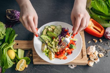 Bir kadın taze sebzelerden vejetaryen salatası yiyor, siyah bir mutfak masasında yakın plan bir tabak. Sağlıklı beslenme konsepti. Evde yemek pişirmek..