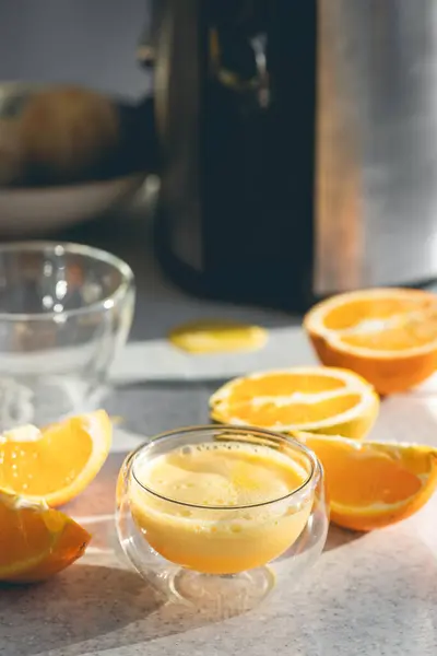 A glass of freshly squeezed orange juice and halves of oranges on the kitchen table. Making freshly squeezed orange juice at home.