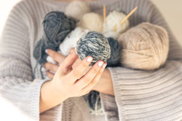 Крупный план, женские руки в шерстяном свитере с несколькими цветными шариками ниток. Женское хобби вязание.