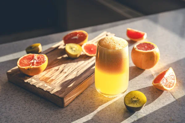 A glass of freshly squeezed juice and fresh fruit on a wooden cutting board on the kitchen table. Squeezed fruit juice at home.